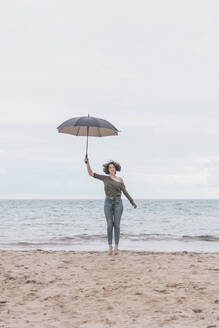 Young woman jumping on the beach, holding umbrella - FVSF00018