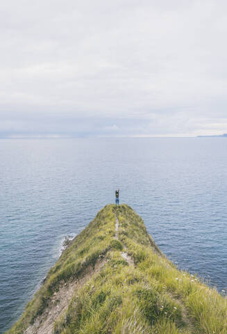 Young woman standing on grass at the cost, looking at the sea stock photo