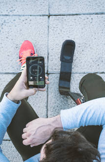 Behinderter Sportler mit Beinprothese, der eine Trainingspause einlegt und sein Mobiltelefon mit Daten versorgt - DAMF00302