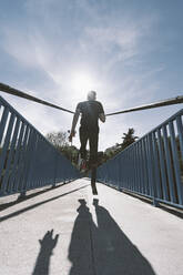 Rückansicht eines behinderten Sportlers mit Beinprothese beim Laufen auf einer Brücke - DAMF00306