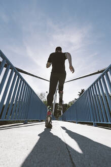 Rückansicht eines behinderten Sportlers mit Beinprothese beim Laufen auf einer Brücke - DAMF00307