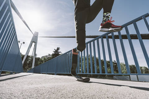 Tiefschnitt eines behinderten Sportlers mit Beinprothese beim Laufen auf einer Brücke, lizenzfreies Stockfoto