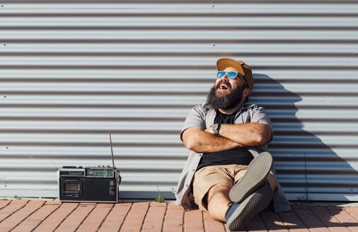 Porträt eines bärtigen Mannes mit Kofferradio, der das Sonnenlicht genießt - JCMF00547