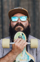 Porträt eines bärtigen Mannes mit Skateboard und verspiegelter Sonnenbrille - JCMF00557