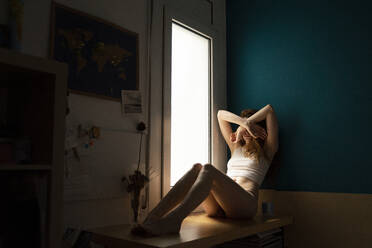 Side view of naked woman looking at camera and sitting in wooden cabinet in  cozy room at home stock photo