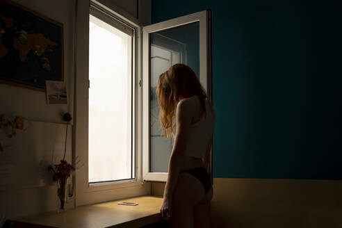 Junge Frau steht am Fenster zu Hause - AFVF05949