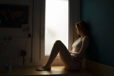 Serious young woman sitting on windowsill at home - AFVF05951