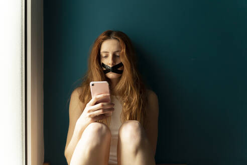 Young woman with taped mouth using cell phone - AFVF05953