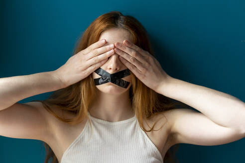 Portrait of young woman with taped mouth covering her eyes - AFVF05954