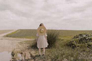 Frau mit Strohhut und Vintage-Kleid allein auf einem abgelegenen Feld auf dem Lande - ERRF03060