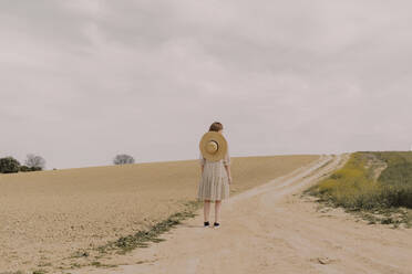Frau mit Strohhut und Vintage-Kleid allein an einem abgelegenen Feldweg auf dem Lande - ERRF03068