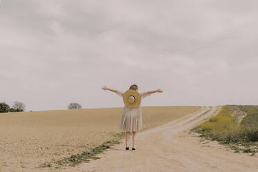 Frau mit Strohhut und Vintage-Kleid allein an einem abgelegenen Feldweg auf dem Lande - ERRF03069