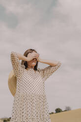 Woman in vintage dress alone at a remote field in the countryside covering her eyes - ERRF03075