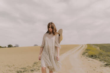 Serious woman in vintage dress walking on a remote field road in the countryside - ERRF03077