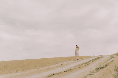 Frau mit Strohhut und Vintage-Kleid steht auf einem abgelegenen Feld auf dem Lande, lizenzfreies Stockfoto
