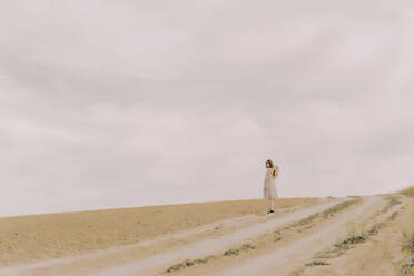 Frau mit Strohhut und Vintage-Kleid steht auf einem abgelegenen Feld auf dem Lande - ERRF03082