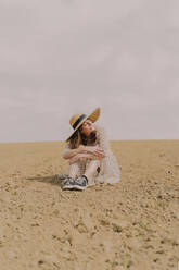 Frau mit Strohhut und Vintage-Kleid sitzt auf einem abgelegenen Feld auf dem Lande - ERRF03087