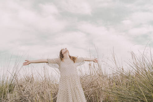 Frau in Vintage-Kleid mit ausgestreckten Armen auf einem abgelegenen Feld auf dem Lande - ERRF03107