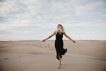 Rückenansicht einer blonden Frau, die barfuß auf einer Sanddüne läuft, Algodones Dunes, Brawley, USA - LHPF01218