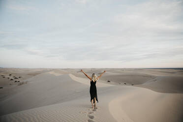 Rückenansicht einer blonden Frau, die auf einer Sanddüne steht und die Hände hebt, Algodones Dunes, Brawley, USA - LHPF01224