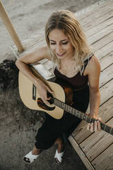 Lächelnde blonde Frau spielt Gitarre im Freien, Kalifornien, USA - LHPF01230