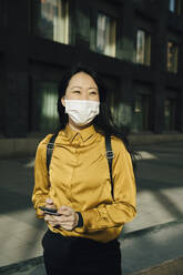 Happy woman with face mask holding smartphone - MASF17316