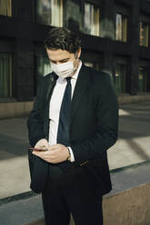 Businessman with face mask using smartphone - MASF17317