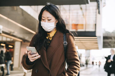 Woman walking in street with face mask using smartphone - MASF17344