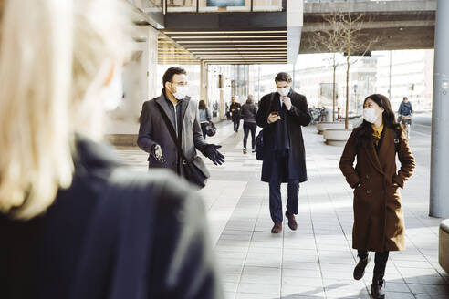 Business people wearing face mask walking in street - MASF17346