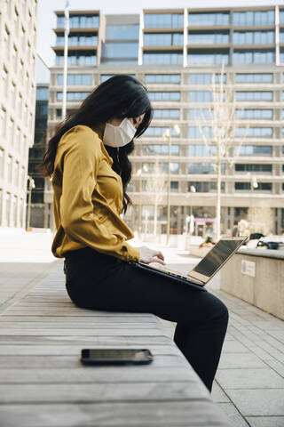 Profil einer Frau mit Gesichtsmaske, die draußen sitzt und arbeitet, lizenzfreies Stockfoto