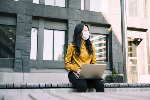 Geschäftsfrau mit Laptop bei der Arbeit im Freien mit Gesichtsmaske, lizenzfreies Stockfoto