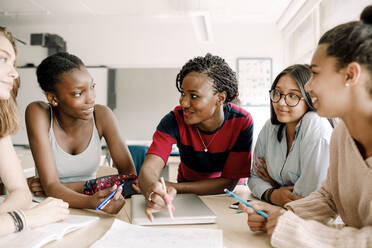 Teacher explaining while smiling teenage students studying by table in classroom - MASF17372