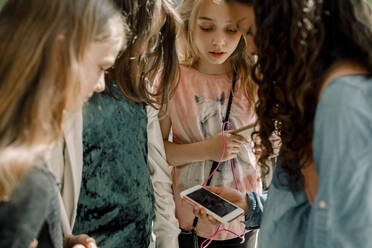 Female students looking at phone while standing in school corridor - MASF17386