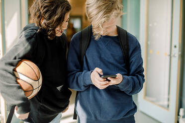 Männliche Schüler benutzen ein Smartphone im Schulflur - MASF17405