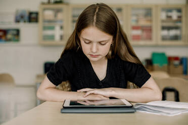Weibliche Schülerin schaut auf ein digitales Tablet, während sie im Klassenzimmer sitzt - MASF17407