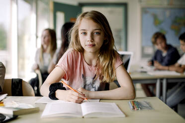 Porträt einer Schülerin, die in ein Buch schreibt, während sie am Tisch im Klassenzimmer sitzt - MASF17408