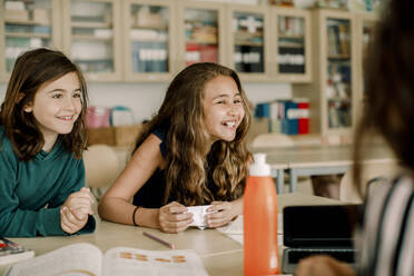 Lächelnde Studentin mit Papier, die neben einem Freund im Klassenzimmer sitzt - MASF17409