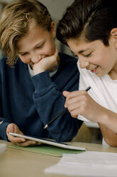 Männlicher Schüler, der auf ein digitales Tablet zeigt, während er mit einem Freund im Klassenzimmer sitzt - MASF17410