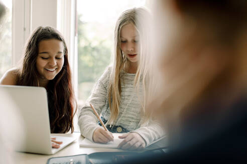 Studentin schreibt in ein Buch, während sie mit einem Freund am Tisch sitzt - MASF17411