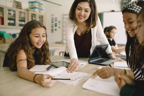 Schüler mit lächelnder Tutorin, die an einem Tisch im Klassenzimmer aus einem Buch lernen - MASF17417
