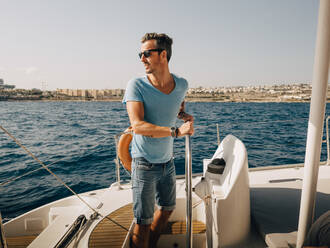 Mature man wearing sunglasses sailing boat in sea against sky - MASF17423