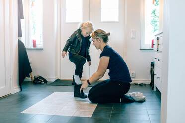 Mother helping daughter with shoes near door at home - MASF17432