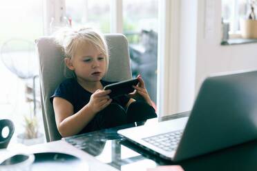 Girl surfing net in smart phone while sitting by table at home - MASF17433