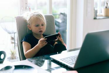 Mädchen surft im Internet auf ihrem Smartphone, während sie zu Hause am Tisch sitzt - MASF17433