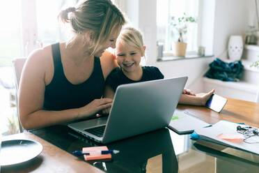 Daughter looking at laptop while sitting by mother at home - MASF17435