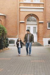 Full length of father and daughter walking home from school in city - MASF17462