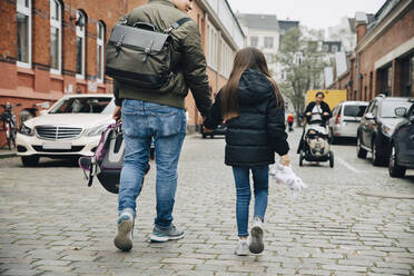 Rückansicht von Vater und Tochter, die sich an den Händen halten, auf einem Fußweg in der Stadt - MASF17465