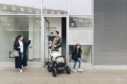 Mutter winkt Vater und Kindern mit Kinderwagen zu, während sie auf dem Bürgersteig in der Stadt spazieren gehen - MASF17469