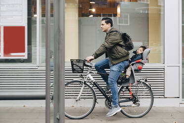 Vater fährt in voller Länge mit seinem Sohn auf dem Bürgersteig in der Stadt Fahrrad - MASF17470