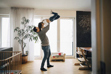 Full length of playful father lifting his daughter while standing in living room - MASF17473